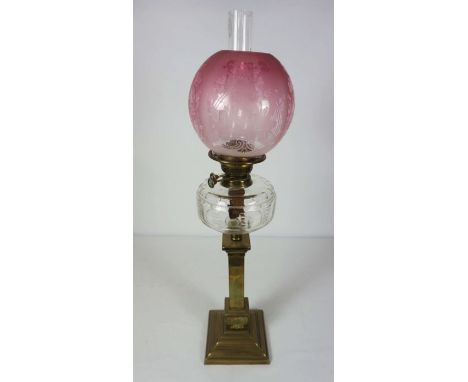 A Victorian brass column oil lamp, circa 1870, with a cranberry glass shade, clear reservoir and the square column with wreat