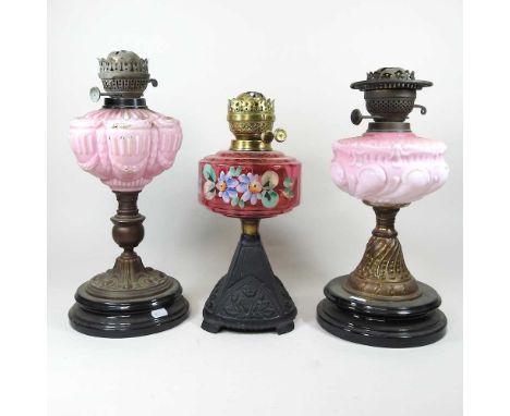A Victorian oil lamp base, with a ruby glass font painted with flowers, 34cm high, together with two others with pink glass f
