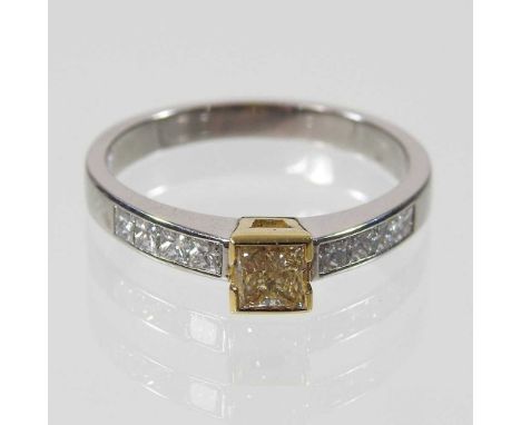 An 18 carat fancy yellow diamond ring, the princess cut central stone, flanked by eight white diamond shoulders, 4.8g, size S