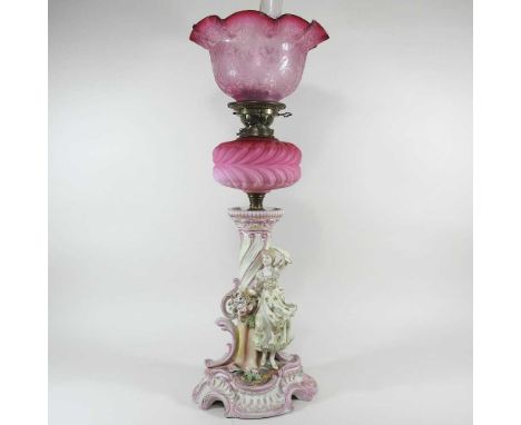 A 19th century continental porcelain figural oil lamp, with a pink glass reservoir and etched cranberry glass shade, 70cm hig