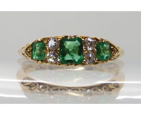 AN 18CT GOLD EMERALD AND DIAMOND RING IN A SCROLLED MOUNT hallmarked Chester 1903, largest emerald 4.7mm x 4mm x 2.5mm, diamo