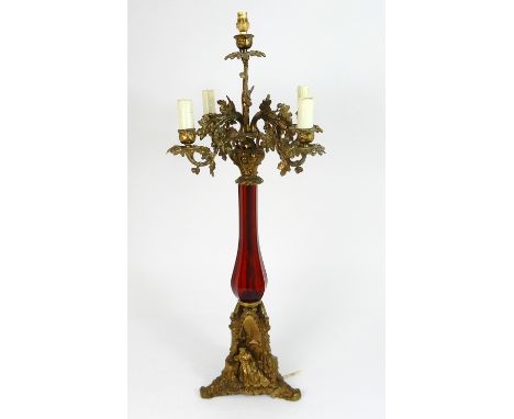 AN ANTIQUE CANDELABRA TABLE LAMP with red glass vase shaped body with acorn and oak leaf moulded candlearms, the triform base