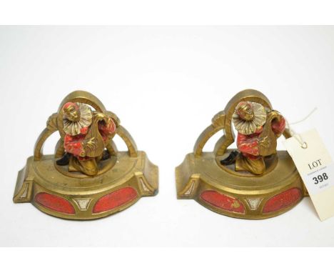A pair of Art Deco brass enamelled bookends, each modelled with a figure of a clown playing a musical instrument, with foundr