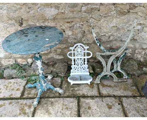 A garden table, with a cast iron base and a marble top, 60 cm diameter, a pair of bench ends, and a stick standWeathered 