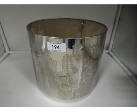 A metal bodied light shade with pressed city scape design