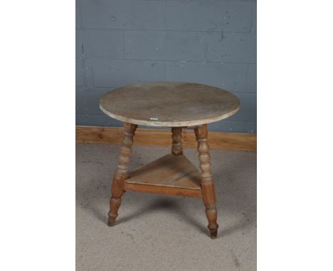 Stripped pine cricket table, the circular top above an under tier and raised on three legs, 74cm diameter