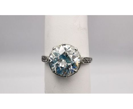 An Edwardian diamond and white metal (tested as platinum) flanked solitaire ring. Set to centre with a round old cut diamond,