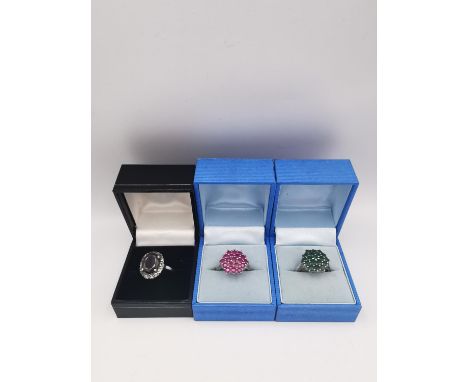 Three silver gem set rings, a ruby cluster ring, an emerald cluster ring and a white metal garnet cluster ring. All ring size