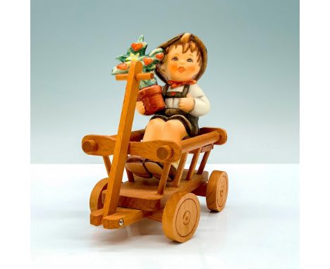 A figure of a young boy wearing a white shirt and brown overalls holding a potted plant with a wooden wagon that he can be pl