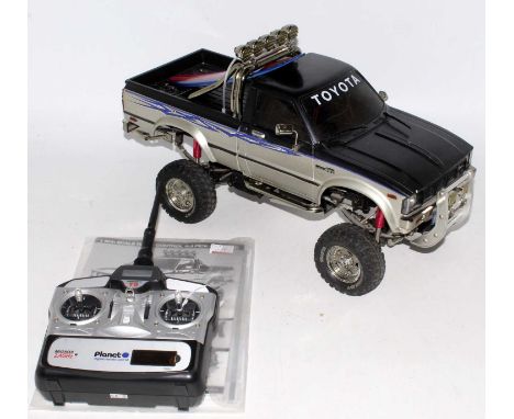 A Tamiya 1/10 scale radio controlled kit built model of a Toyota Hilux Hi-lift pickup truck 4x4 example with surf board acces