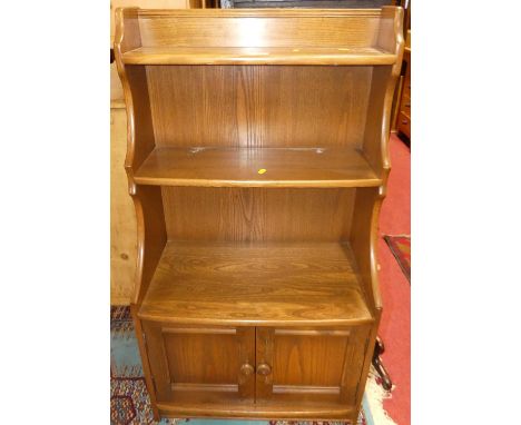 An Ercol mid-elm bow front waterfall bookshelf, having twin lower cupboard doors, width 61cm