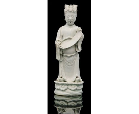 A late 17th Century Chinese blanc de chine heavenly official standing in a loose tunic and unrolling a scroll with a tall cap