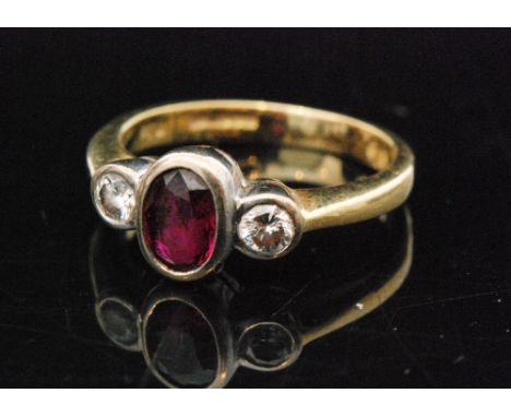 A modern 18ct ruby and diamond three stone ring, central oval ruby flanked by a brilliant cut diamond to each shoulder, all s