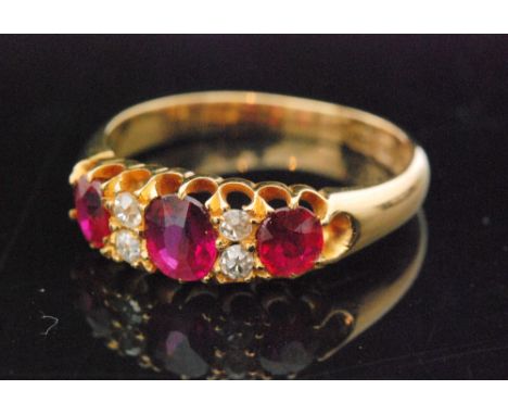 An 18ct ruby and diamond ring, three graduated oval cut rubies spaced by four diamonds to pierced mount and tapering band, ri