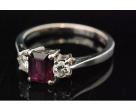 A ruby and diamond three stone ring, two brilliant cut diamonds beside central emerald cut ruby, to plain platinum chenier ba