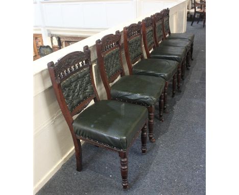 A set of six Victorian carved dining chairs with green leather button upholstered backs and stuff over seats on turned legs a