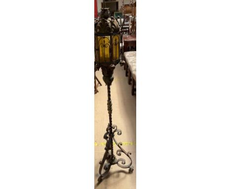 A wrought iron standard lamp with coloured glass panels and a twist column with scrolling feet