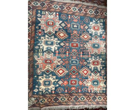 A rug with a light blue ground and geometric patterns together with two prayer rugs