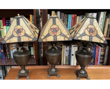 A set of three bronze vase and pineapple table lamps on paw feet with Tiffany style shades