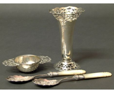 A small silver candlestick holder with pierced decoration, silver tea strainer and two silver spoons with mother of pearl han