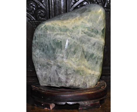 A large jade coloured hardstone rock specimen on woodstand