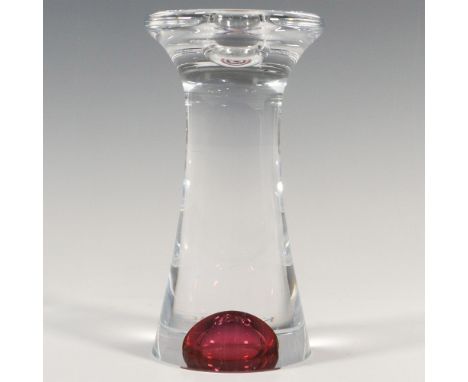 A clear abstract form candlestick holder accented with a dark-pink glass bubble at the bottom. Kosta Boda and artist's name e