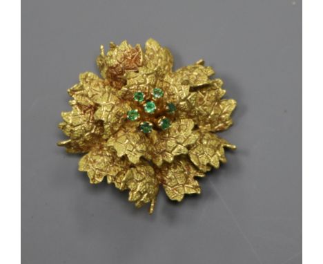 A continental 18k yellow metal and emerald set flower head brooch, 35mm.