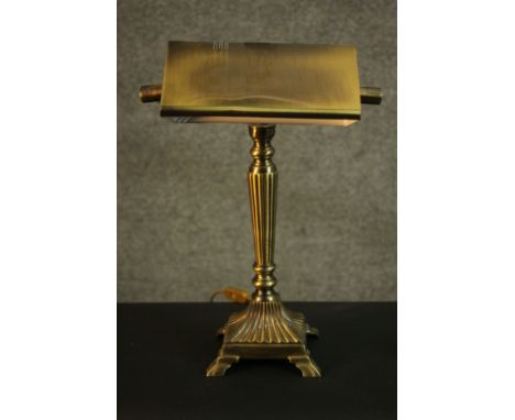 A replica Victorian style banker's brass desk lamp, with a brass shade, a reeded stem on a square reeded base with four feet.