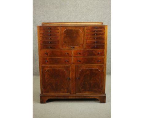 An early 20th century walnut dentists cabinet with a gallery back over a central fall front, flanked by six graduated short d