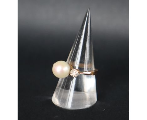 A pearl and diamond ring set with a central pearl approximately 8mm diameter, flanked by a pair of round brilliant cut diamon