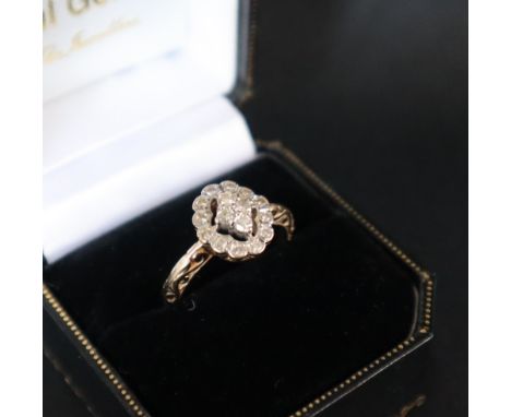 A diamond cluster ring, set with four round cut diamonds to the centre, the oval border set with twelve round old cut diamond