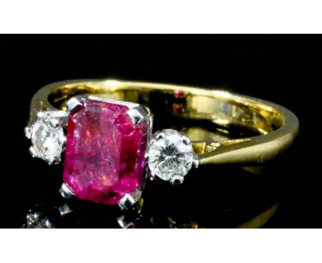 A modern gold coloured metal mounted ruby and diamond three stone ring, set with a rectangular central ruby (approximately .7