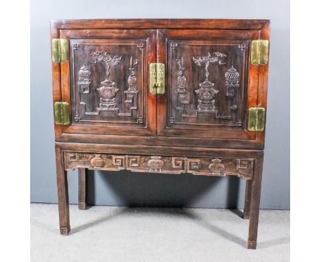 A Chinese panelled hardwood cabinet with flush panel to top, fitted one plate glass shelf enclosed by a pair of doors carved 