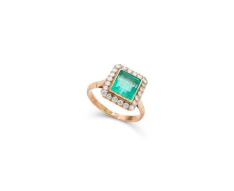 An emerald and diamond cluster ring collet-set with a rectangular step-cut emerald, in a border of small old round-cut diamon