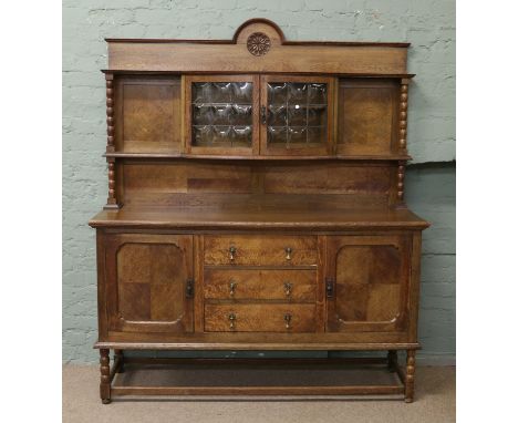 An early C20th carved oak and paneled sideboard with bow shaped glass display and bobbin turned supports 