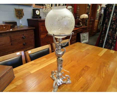 A silver plated oil lamp converted to electric, frosted glass shade over a scrolled stylistic base