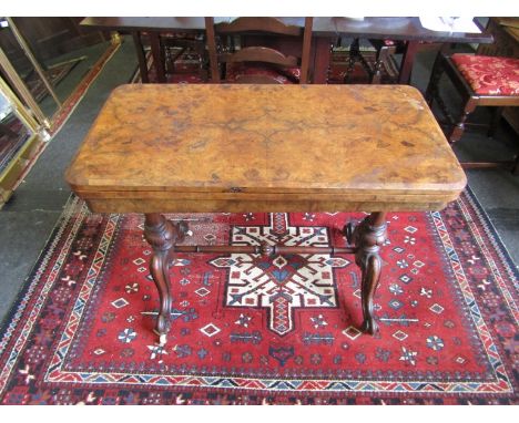 A walnut quarter sawn card table with scrolled feet, turned stretcher and ceramic castors