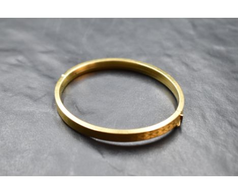 A 9ct gold filled hinged bangle having engine turned decoration and concealed clasp, internal measurements: 65mm x 54mm &amp;