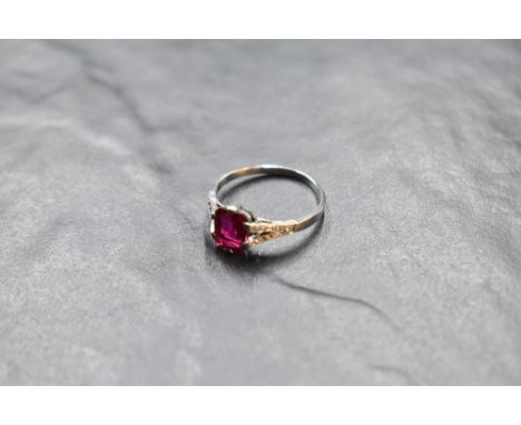 A baguette cut ruby ring, approx 1ct, in a claw set mount, having diamond set split shoulders on a white metal loop stamped 1