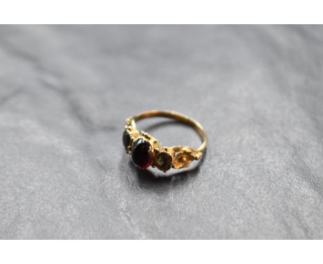 A garnet cabochon ring flanked by two paste stones, all in an ornate mount with filled backs on a yellow metal loop, no marks