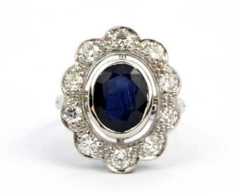 An 18ct white gold (stamped 18k) cluster ring set with an oval cut sapphire surrounded by brilliant cut diamonds, (N).