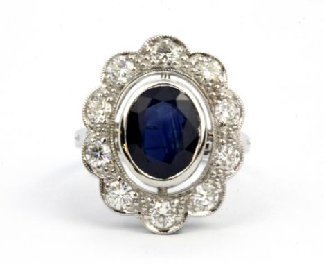 An 18ct white gold (stamped 18k) cluster ring set with an oval cut sapphire surrounded by brilliant cut diamonds, (N).