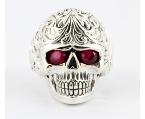A sterling silver skull shaped ring with ruby set eyes, (Q).