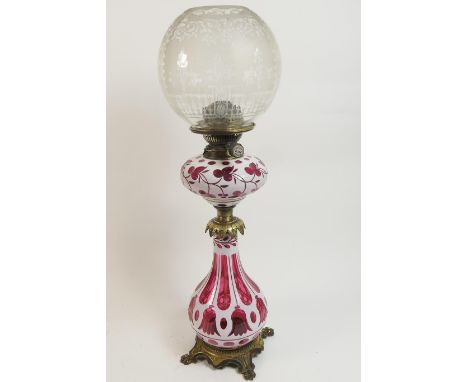 Bohemian ruby and white overlay glass and brass pedestal oil lamp, having an etched spherical shade over an overlay glass tan