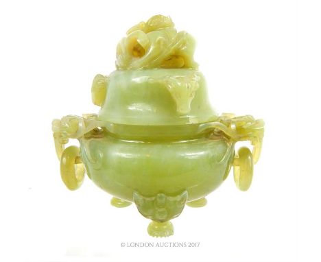 A Chinese jade censar, having a lid, carved with a dragon, the body having twin dragon mask handles, holding hoops, raised on