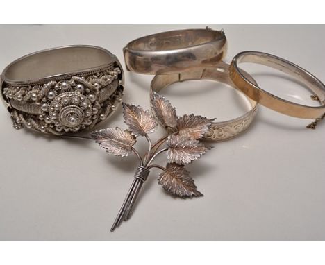 Silver hinged bangle, half engraved, another silver hinged bangle, a strap bangle, another bangle and a leaf-formed brooch, (