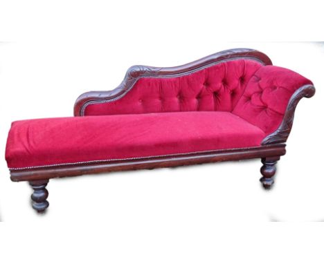 A Victorian mahogany chaise lounge, with a part show frame, upholstered in red button velvet, on turned legs.