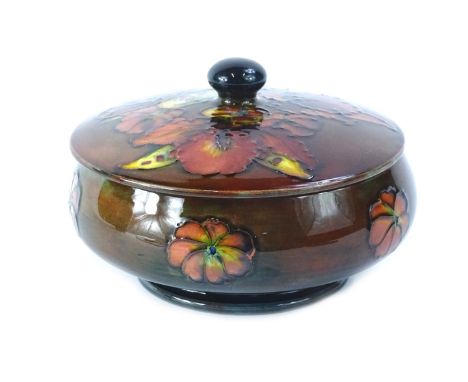 A Moorcroft Flambe Orchid pattern box and cover, on a mottled blue and brown ground, impressed mark and paper label to unders