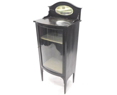 An Edwardian ebonised music cabinet, the raised back with an oval bevelled mirror plate, the base with a single glazed bow fr