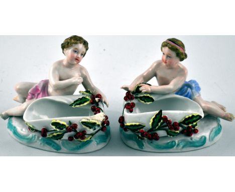 A pair of Continental glazed ceramic salts modelled as cherubs with holly-festooned conch shells (2)